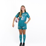 Tina Tinelli wearing her soccer uniform on a white background and holding a soccer ball under one arm.