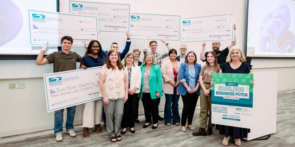 A group of students pose with faculty and hold up large checks.