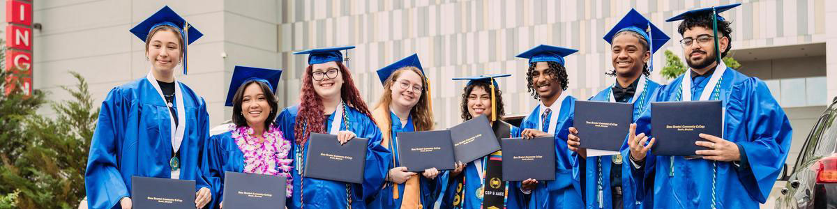 Group of students in cap and gown holding up their degrees