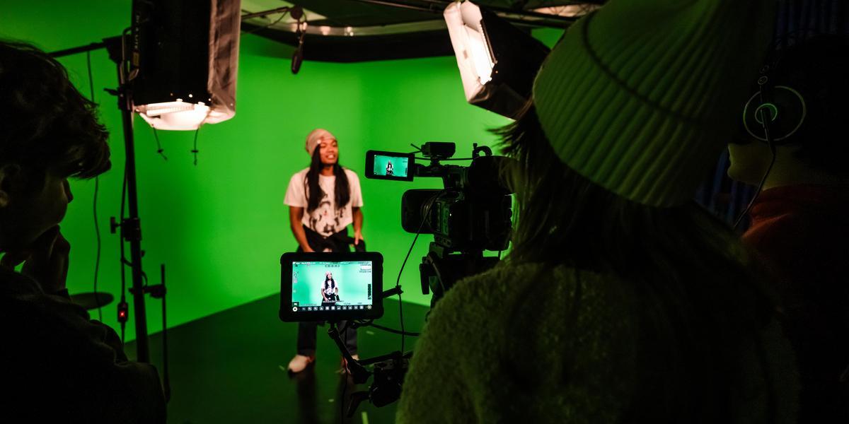 Student filming another student in front of a green screen.