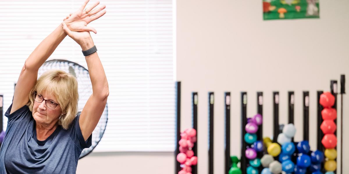 A woman stretching in front of a rack of dumbbells