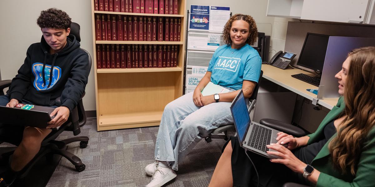 Two people, one wearing an AACC T-shirt, meeting with the director of the Legal Clinic