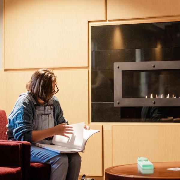 Students on laptops studying in front of fireplace.