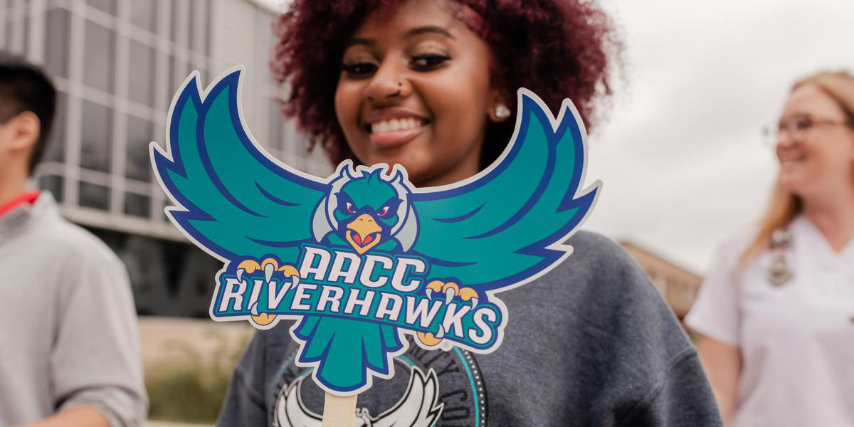 Student holding a cutout of the Riverhawk logo